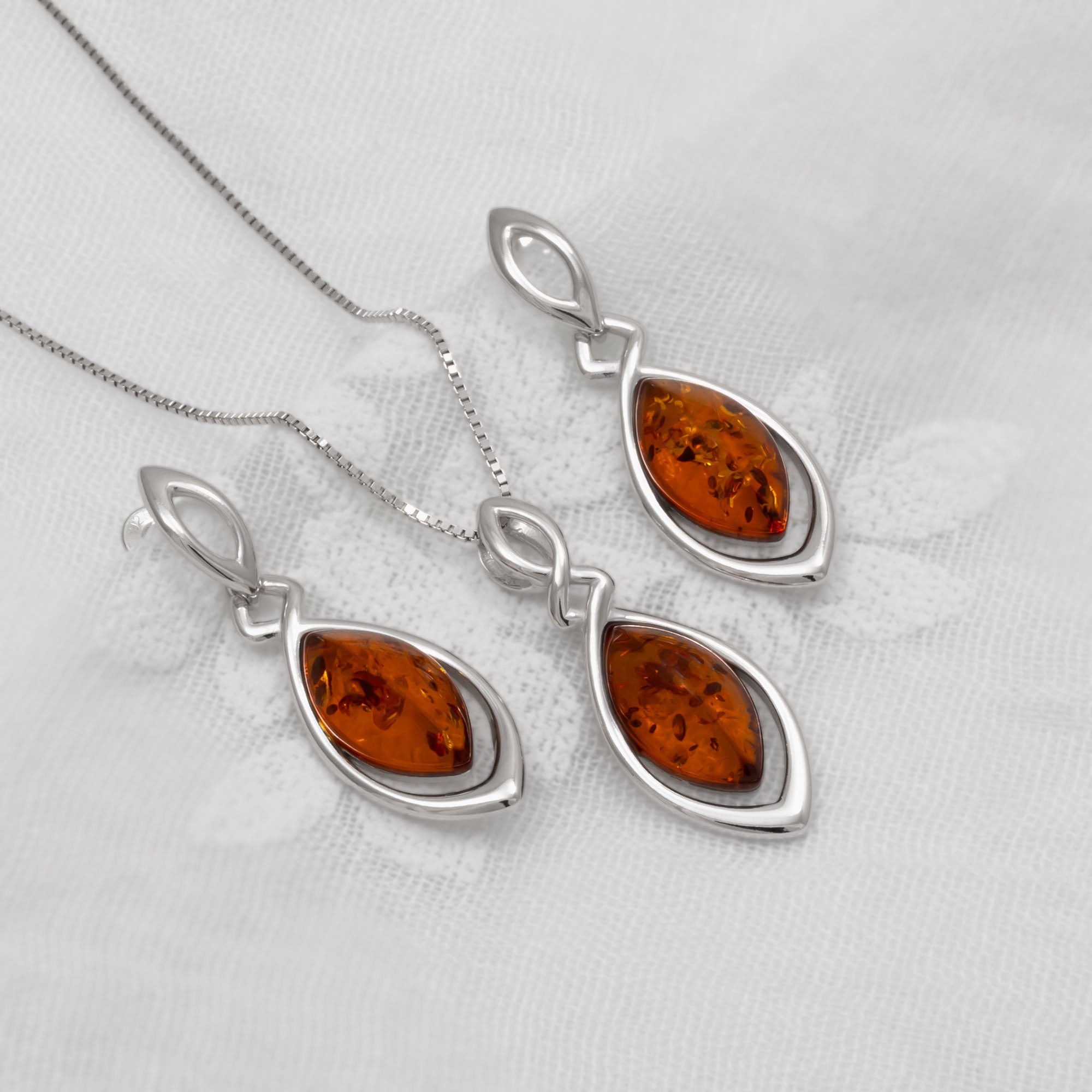 Set of silver pendant and matching earrings with amber stones on a white background