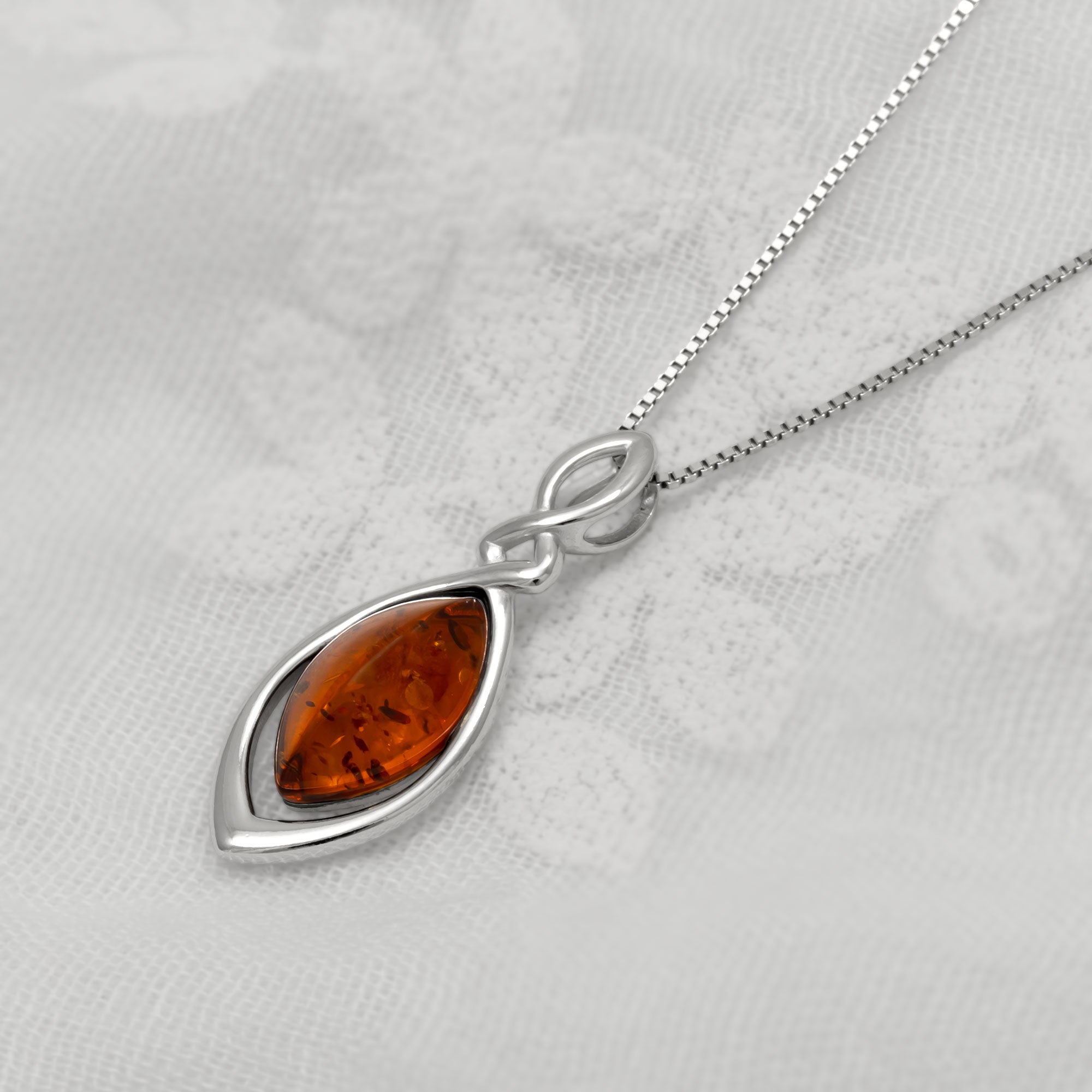 Silver necklace with a amber teardrop pendant on a light gray background