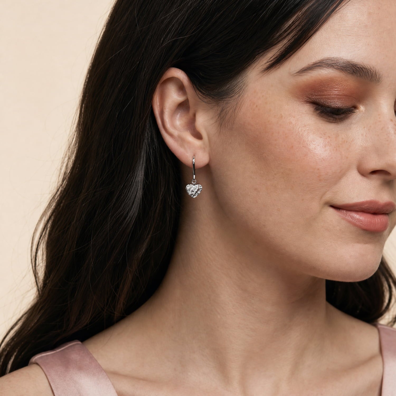 Model wears a pair of textured sterling silver heart-shaped earrings