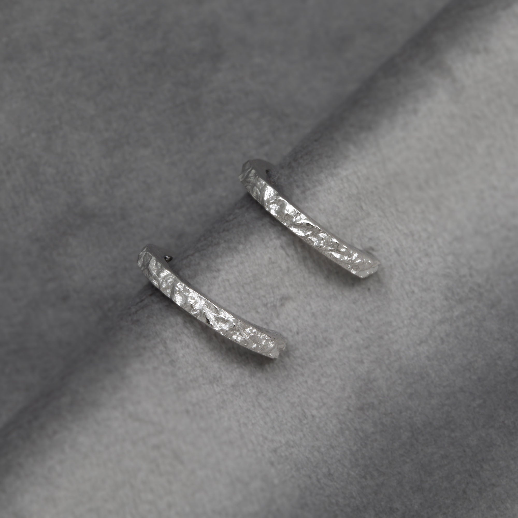 Silver textured hoop earrings on a grey background