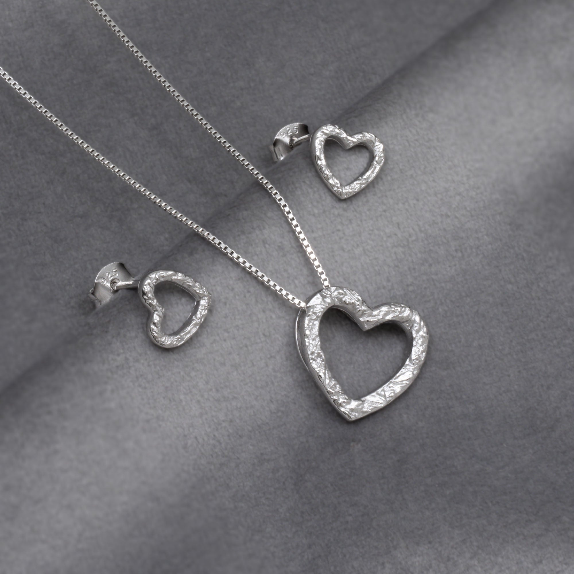 Silver textured heart-shaped necklace and earrings on a grey surface