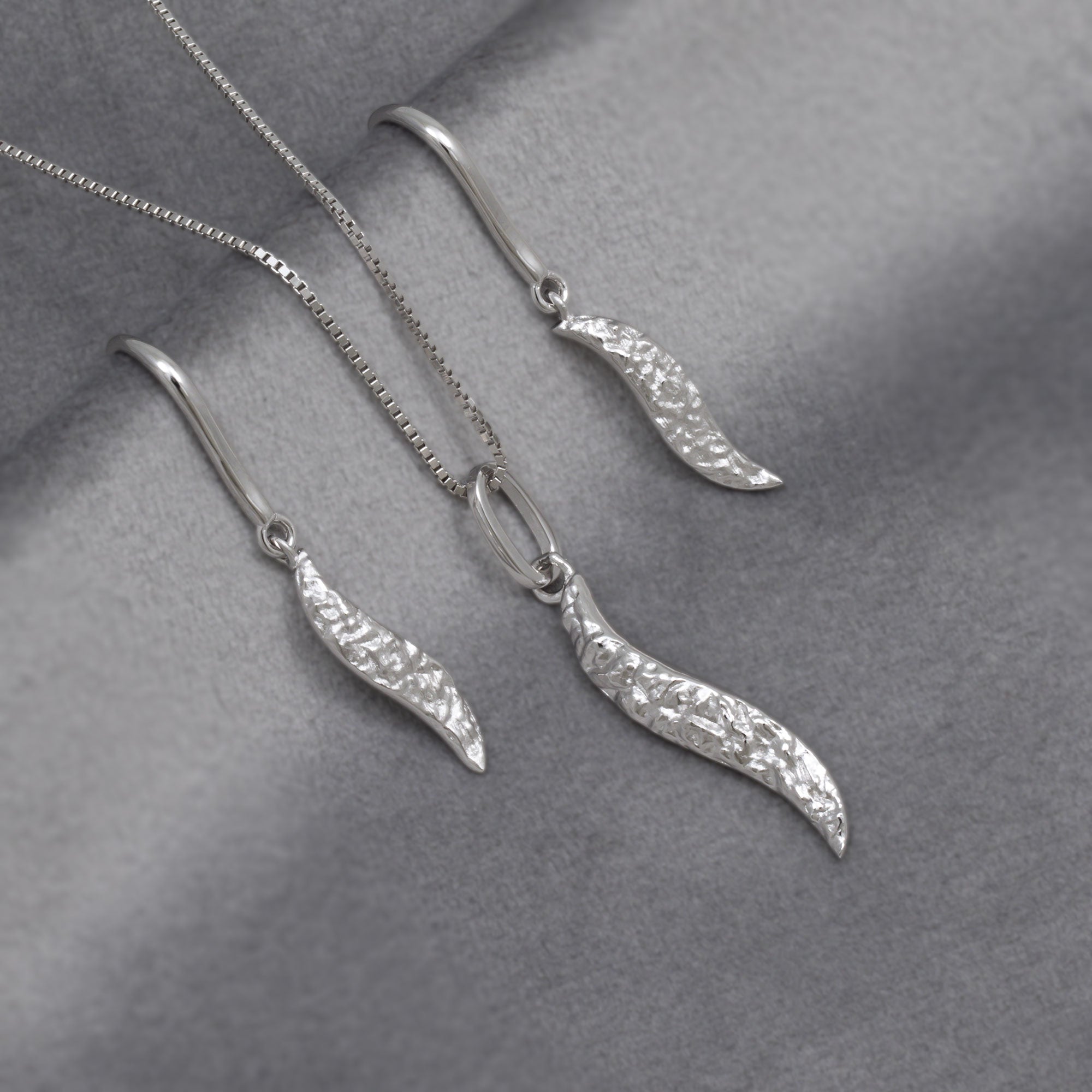 Silver textured leaf-shaped pendant and earrings on a grey surface