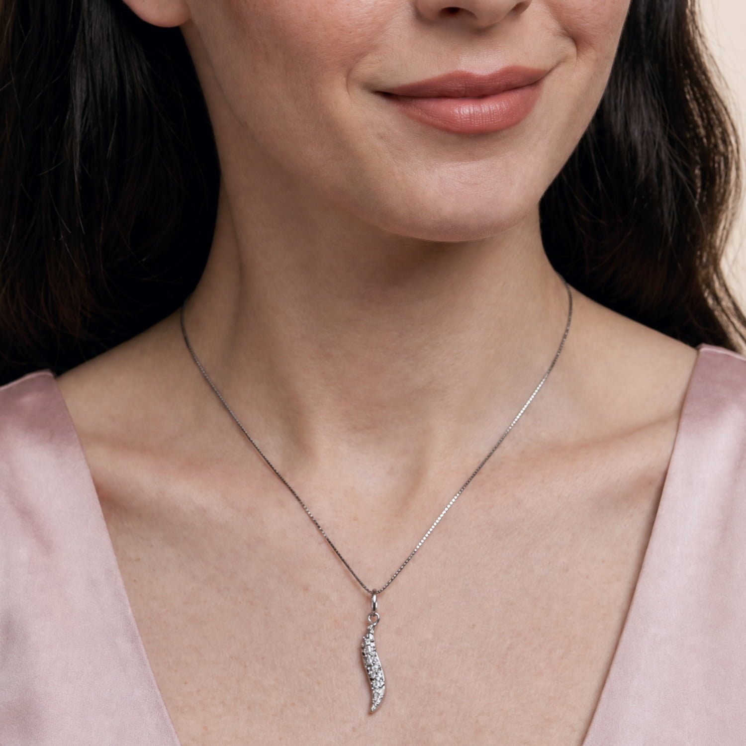 A close-up of a woman wearing a delicate silver chain necklace with a small silver leaf shaped pendant with a textured finish.