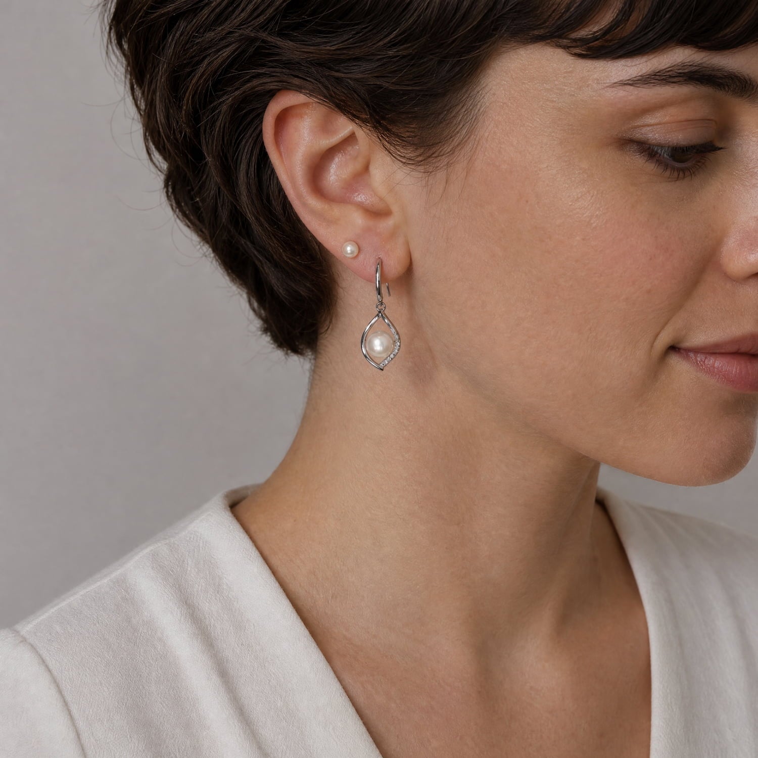 Pair of sterling silver drop earrings featuring an open twist design accented with pavé cubic zirconia stones and a central lustrous freshwater pearl for timeless elegance.