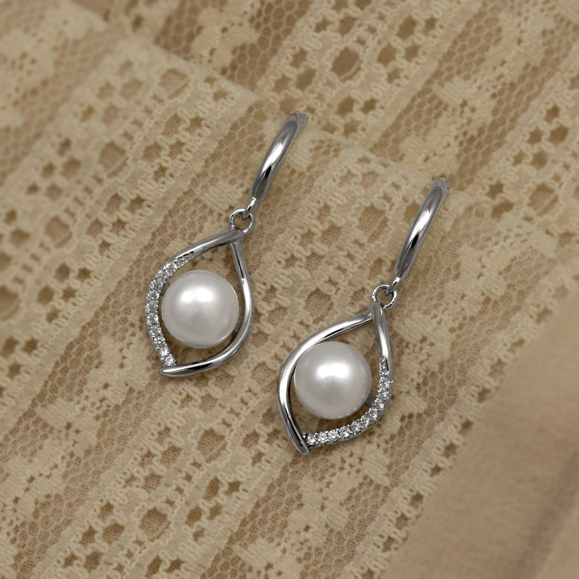 Elegant sterling silver drop earrings featuring an open twisted design accented with pavé cubic zirconia and a luminous freshwater pearl, displayed on delicate lace.