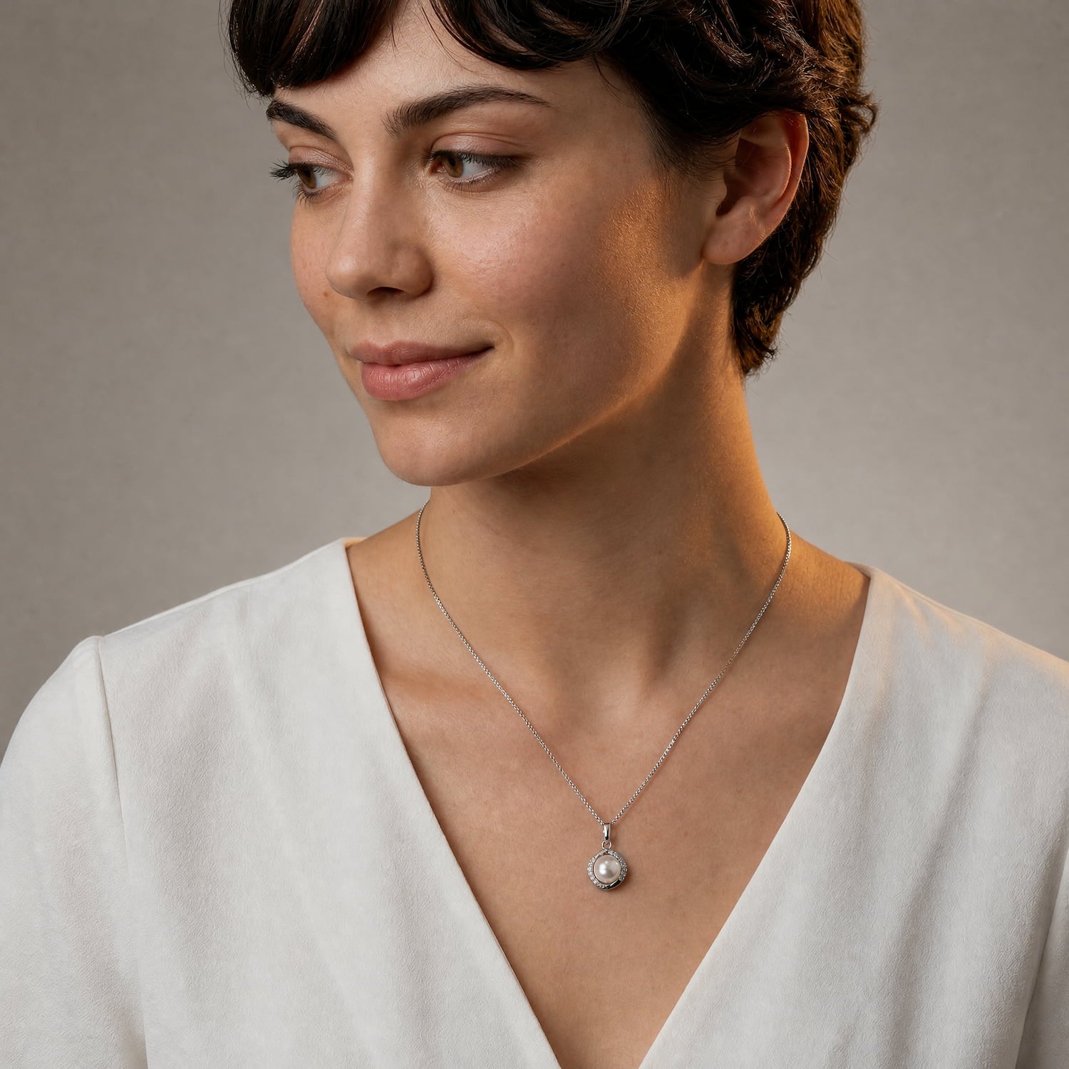 A woman with short dark hair wearing a silver necklace with a round freshwater pearl pendant, accented with cubic zirconia