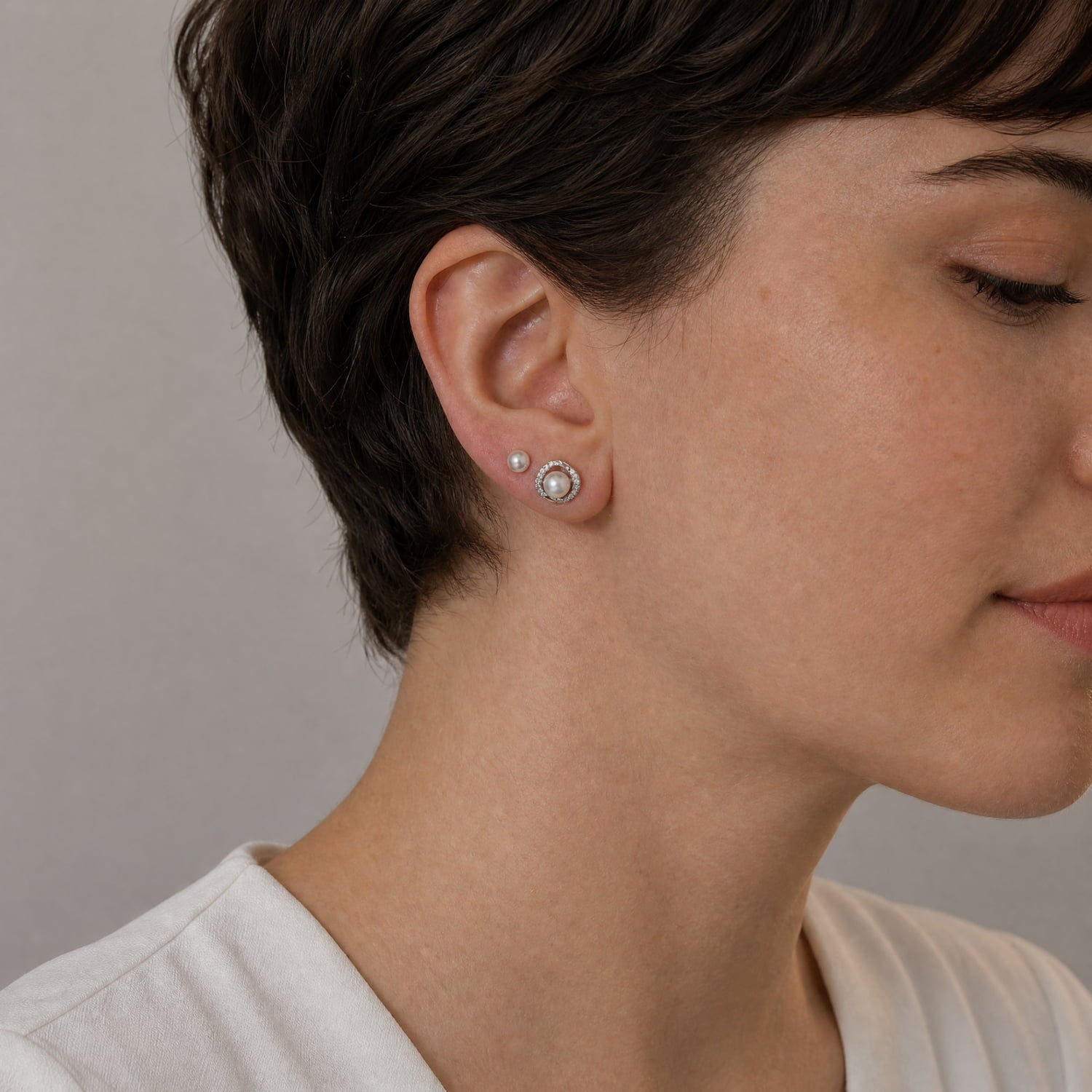 Pair of sterling silver earrings featuring a wraparound pavé cubic zirconia setting encircling lustrous freshwater pearls, combining classic elegance with contemporary design.