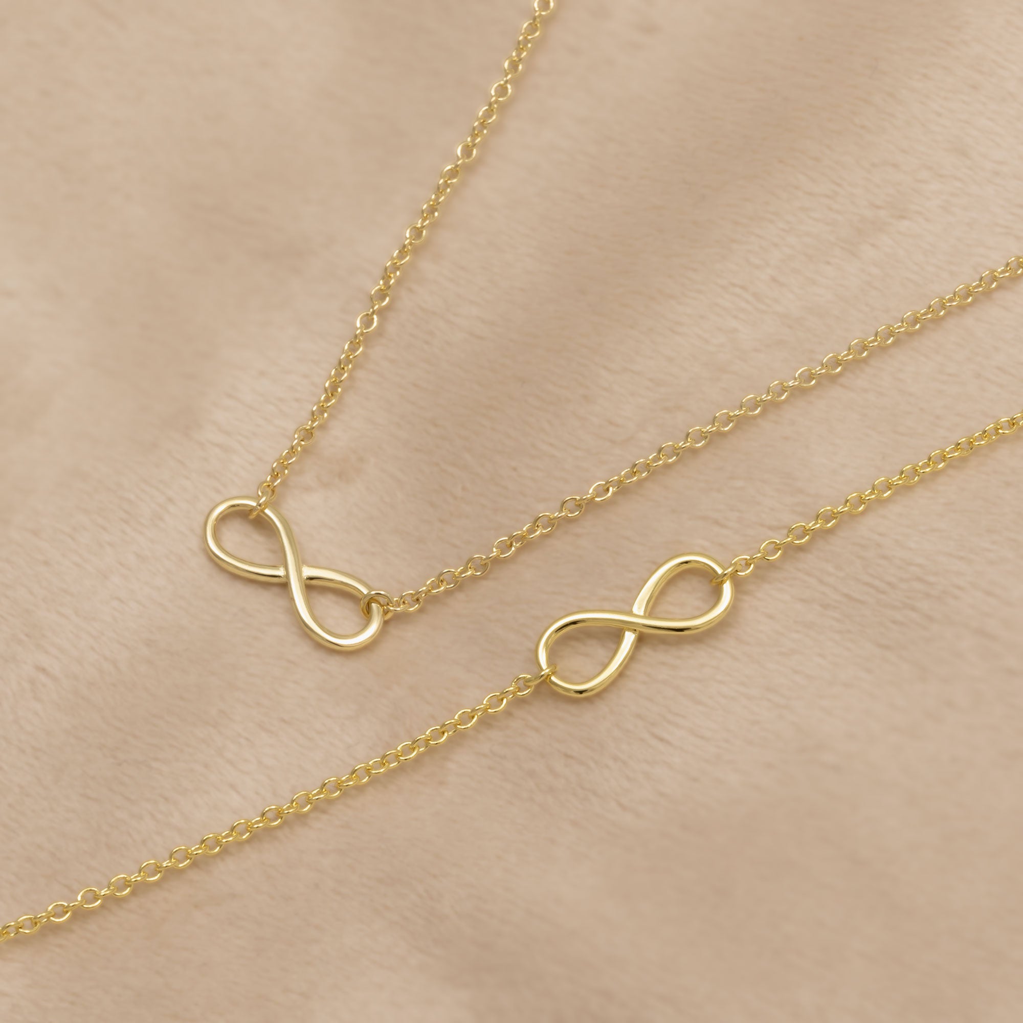 Gold vermeil infinity necklace and bracelet on a beige background