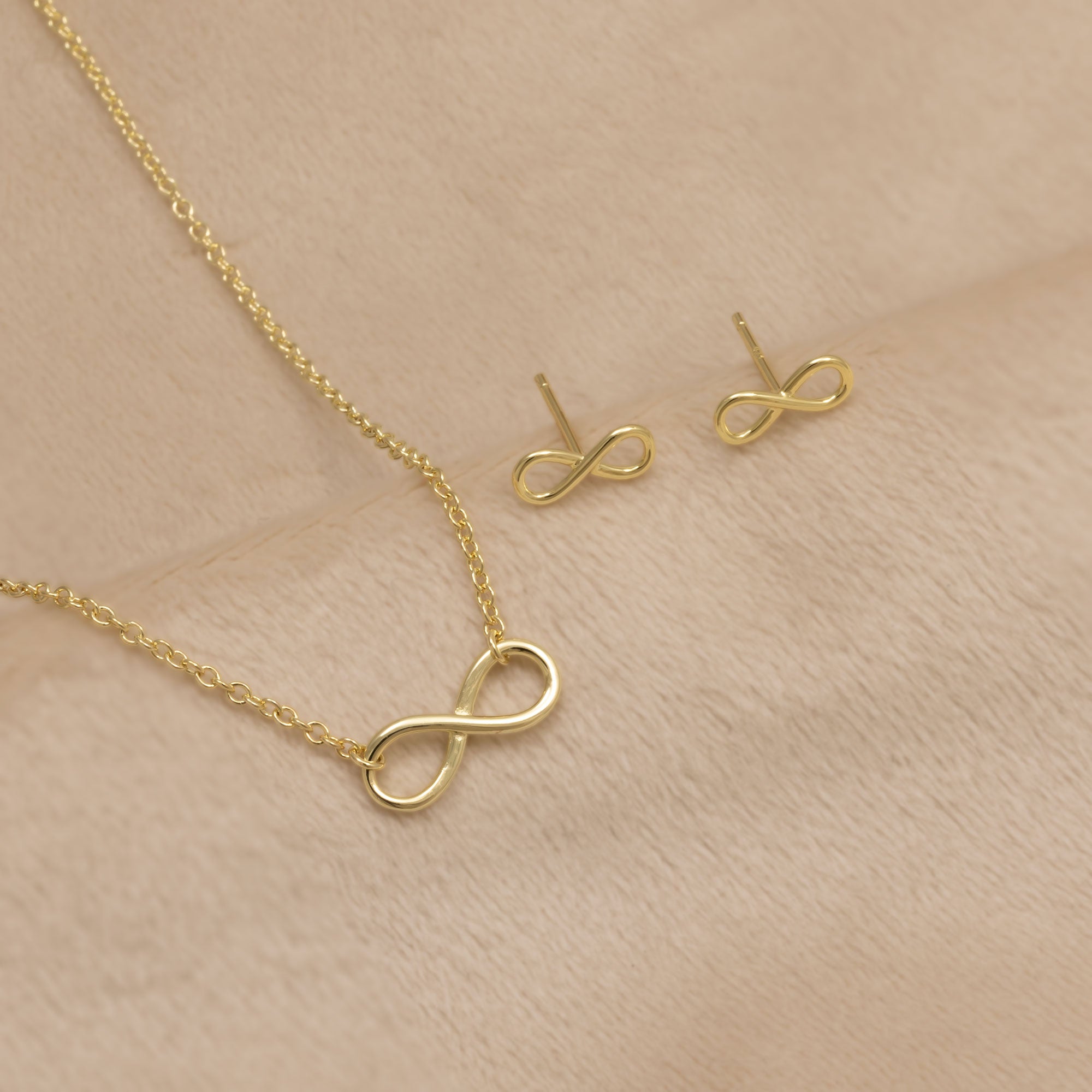 Gold vermeil infinity necklace and stud earrings on a beige background