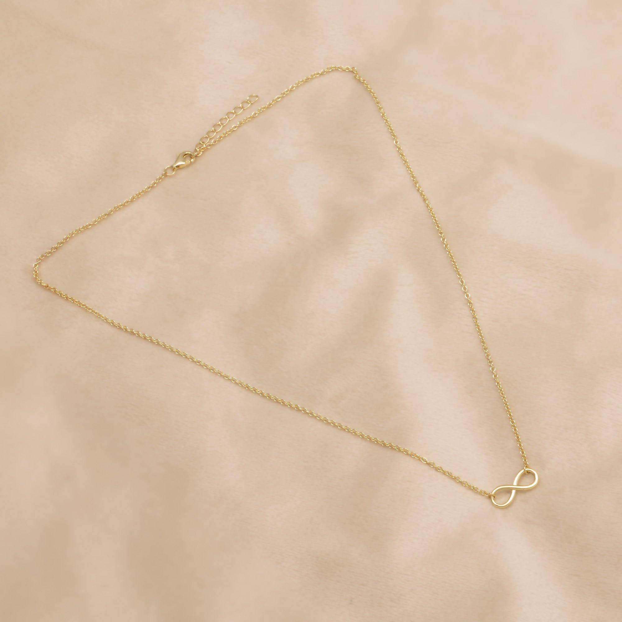 Gold vermeil infinity necklace on a beige background