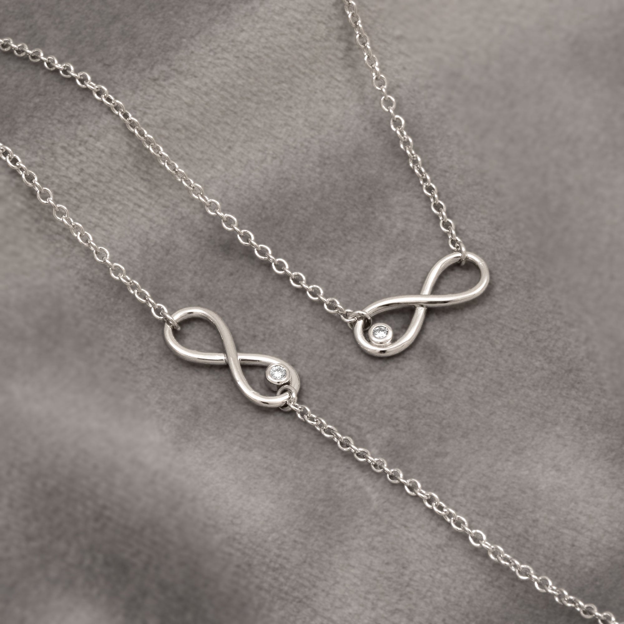 Silver infinity necklace with small diamonds on a gray background