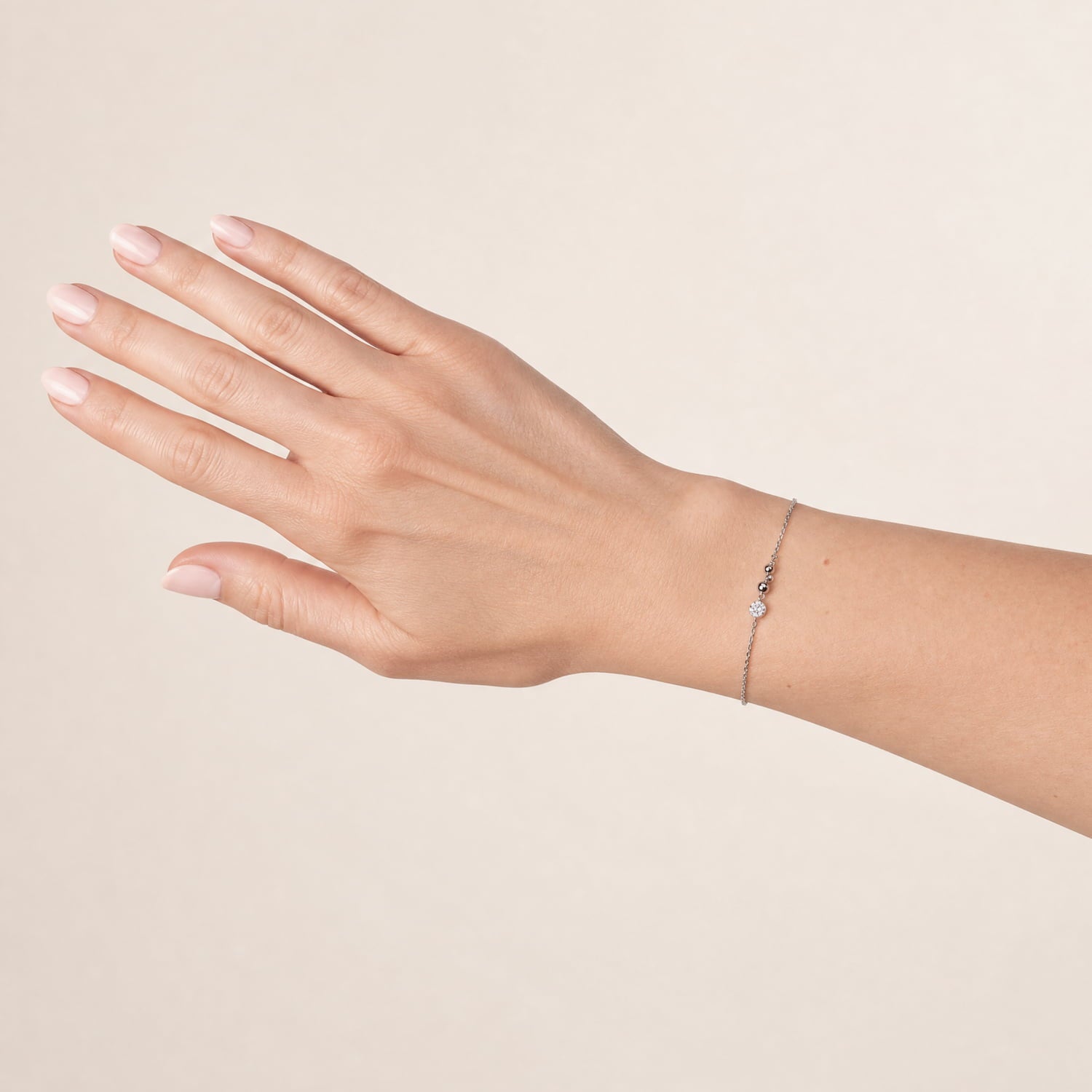 A delicate silver chain bracelet with a small silver beads, shown worn on a woman's wrist against a solid beige background.