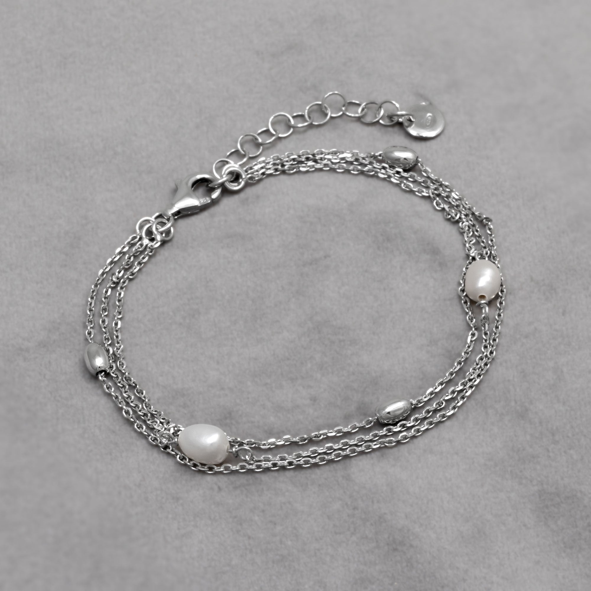 Silver bracelet with multiple chains, freshwater pearls and silver beads on a grey background