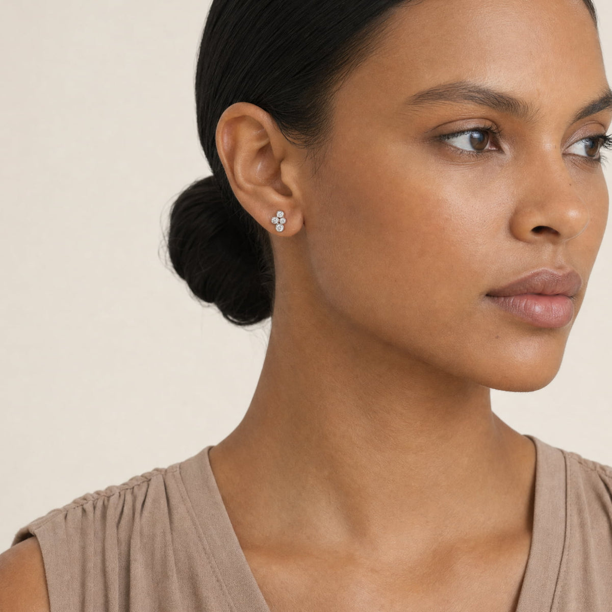 A close-up of a woman wearing a small silver stud earring with clear cubic zirconia stones, shown against a plain light beige background.