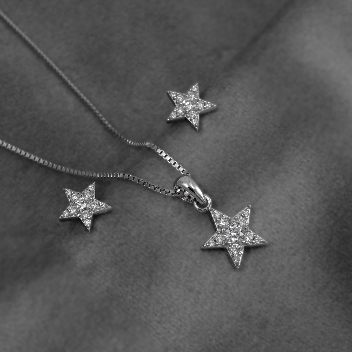 A pendant and a pair of silver star-shaped stud earrings fully set with pavé lab grown diamonds, shown on a grey background.