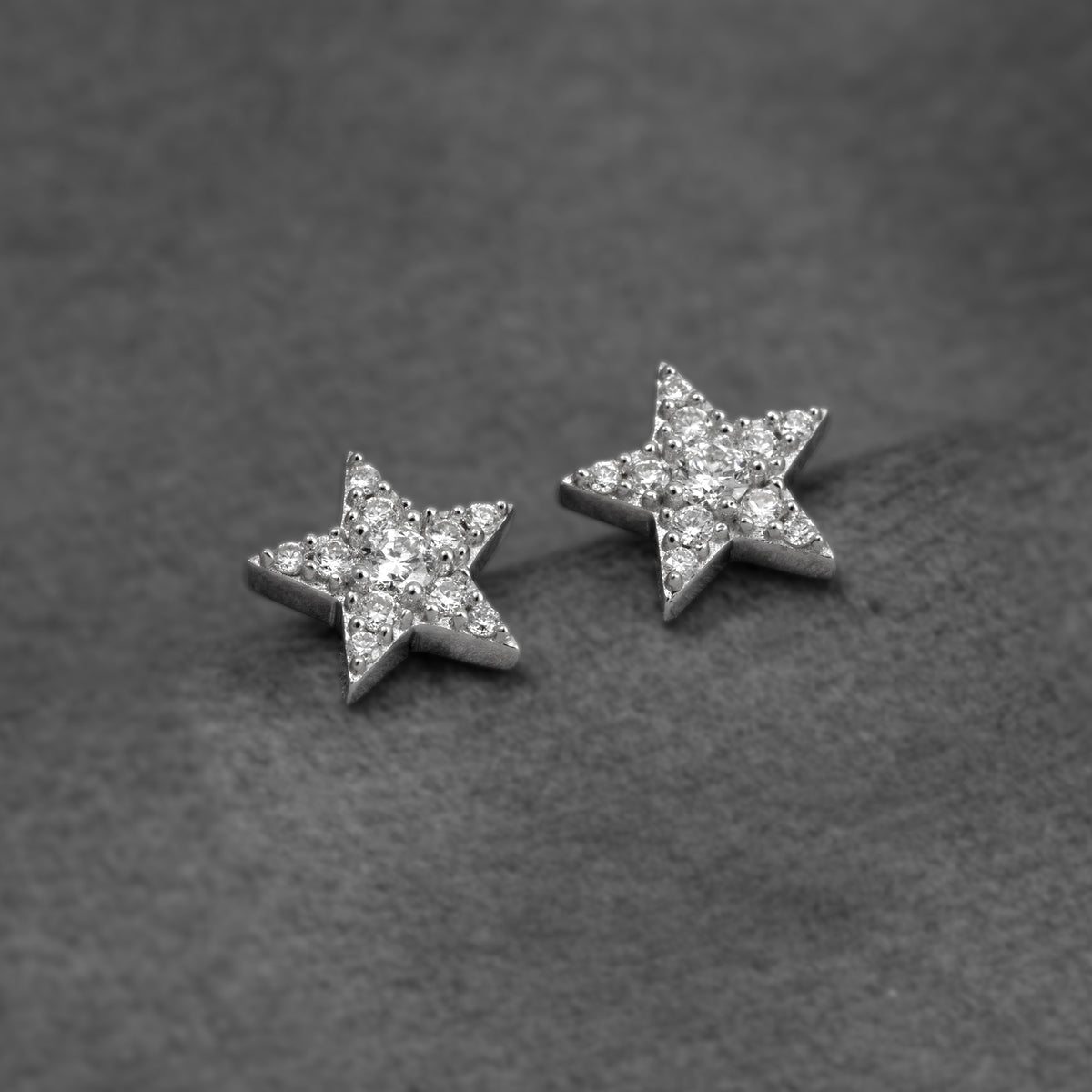 A pair of silver star-shaped stud earrings fully set with pavé lab grown diamonds, shown on a plain grey background.
