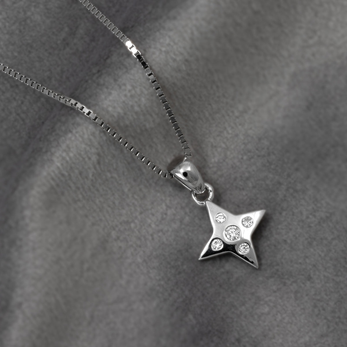A silver star-shaped pendant necklace with five lab grown diamonds, displayed on a textured gray fabric background.