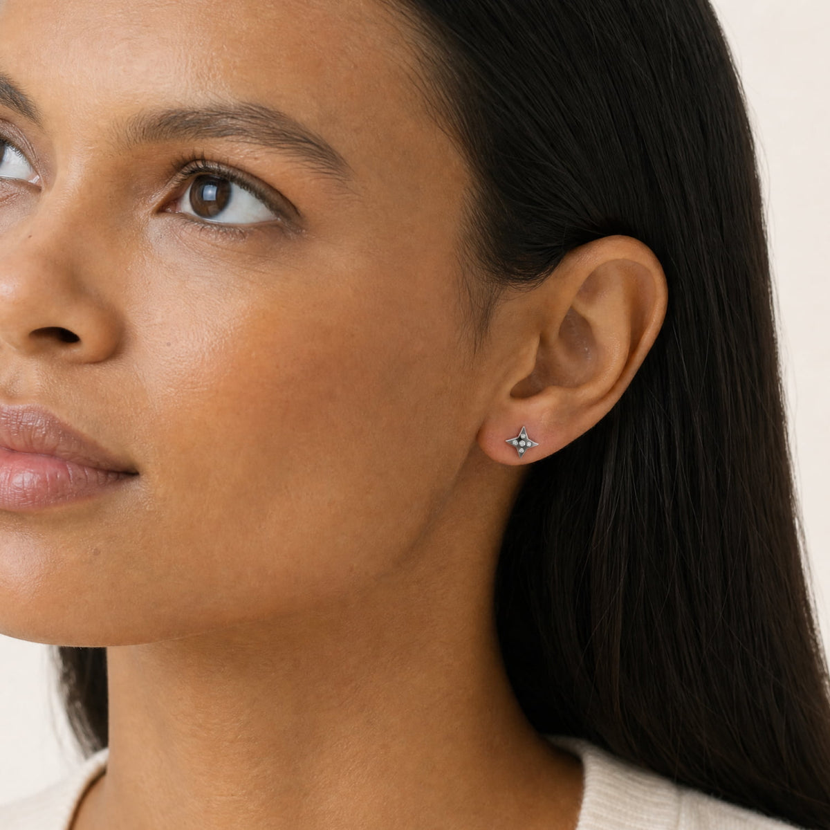Close-up of a woman's ear wearing a small silver star stud earring with lab grown diamonds, shown against a soft light beige background.