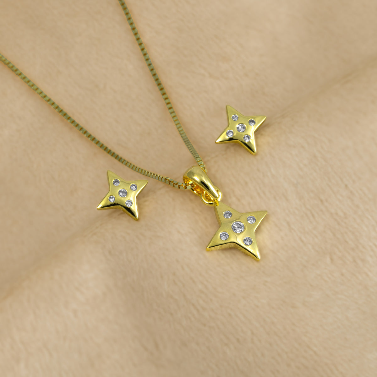 A jewellery set consisting of gold vermeil star-shaped stud earrings and matching pendant, each adorned with five clear lab grown diamonds, set against a plain cream background.