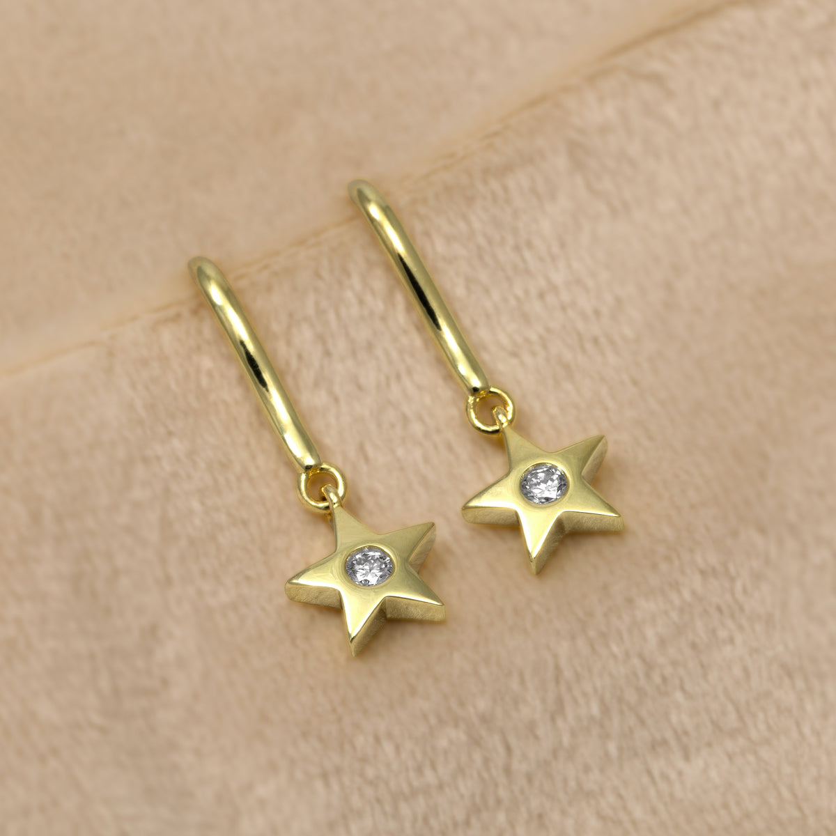 A pair of gold vermeil star-shaped dangle earrings with a lab grown diamond in the centre of each star, shown against a cream background.