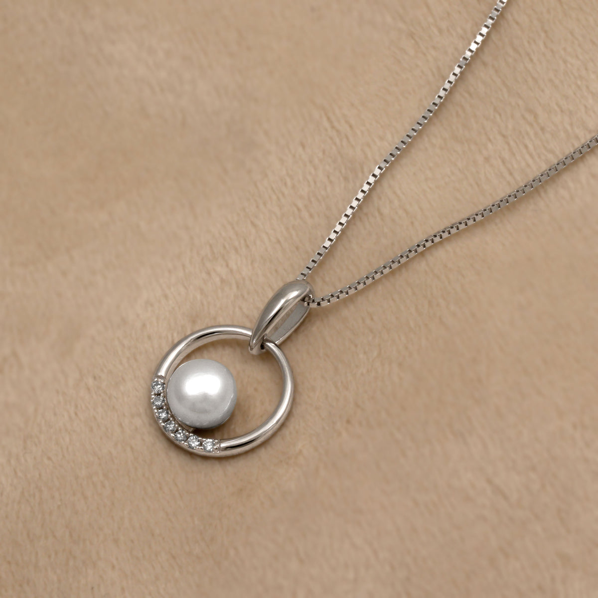Silver circular pendant featuring a pearl and lab grown diamonds on a beige background