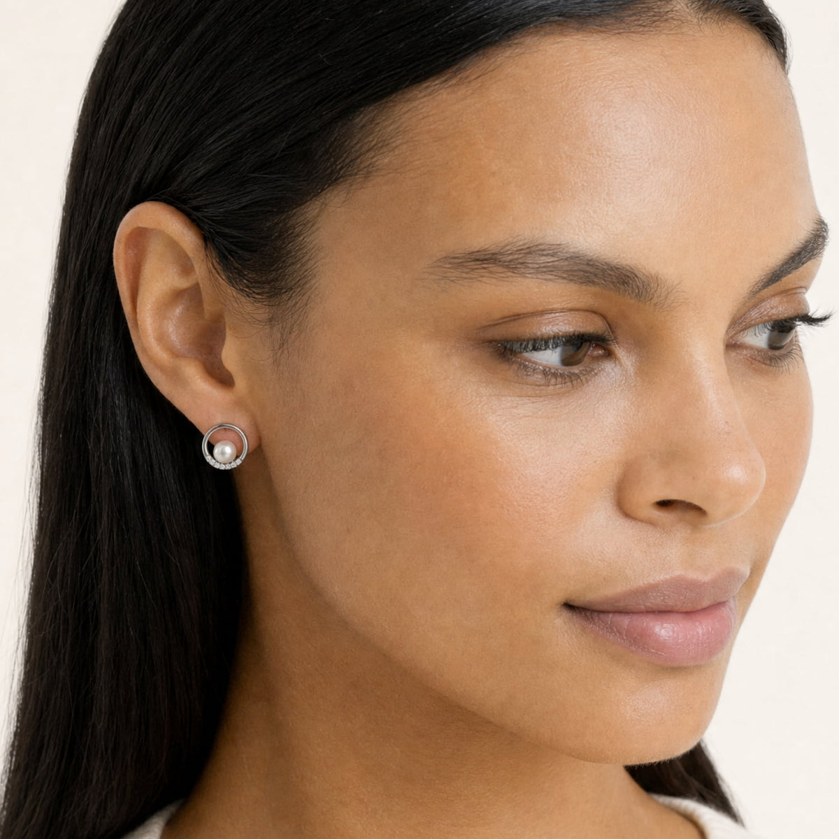 A close-up of a woman wearing a small round silver stud earring with freshwater pearl and lab grown diamonds, shown against a plain light background.