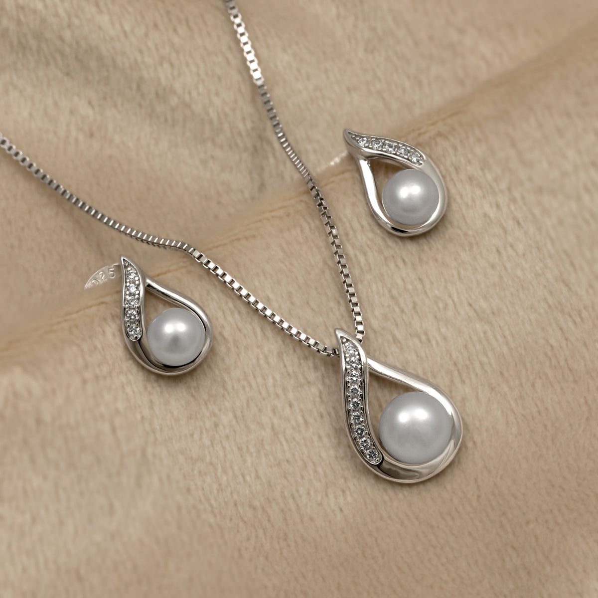 Pearl necklace and earrings set on a beige fabric background