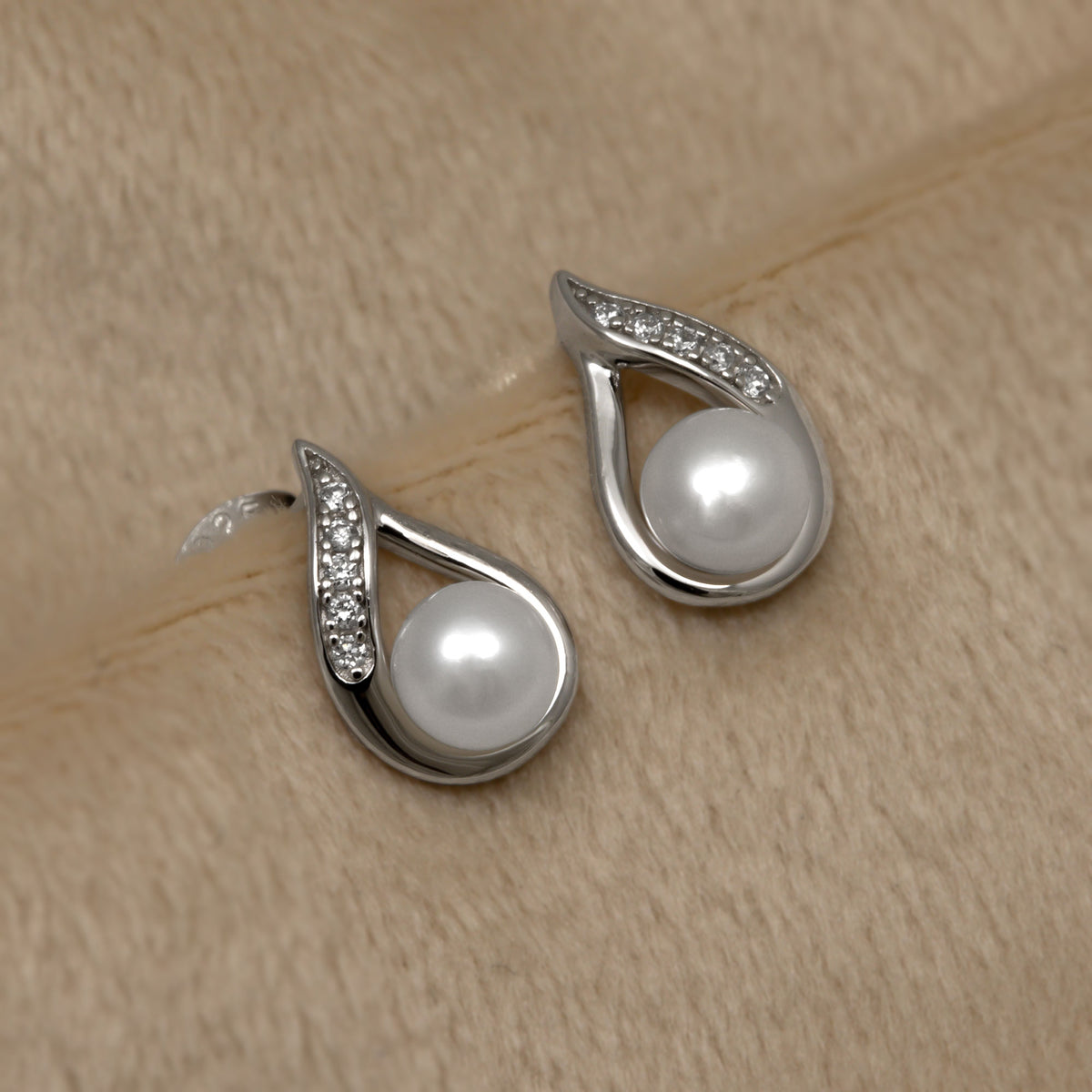 Silver teardrop stud earrigs with freshwater pearl and lab grown diamonds on a beige surface