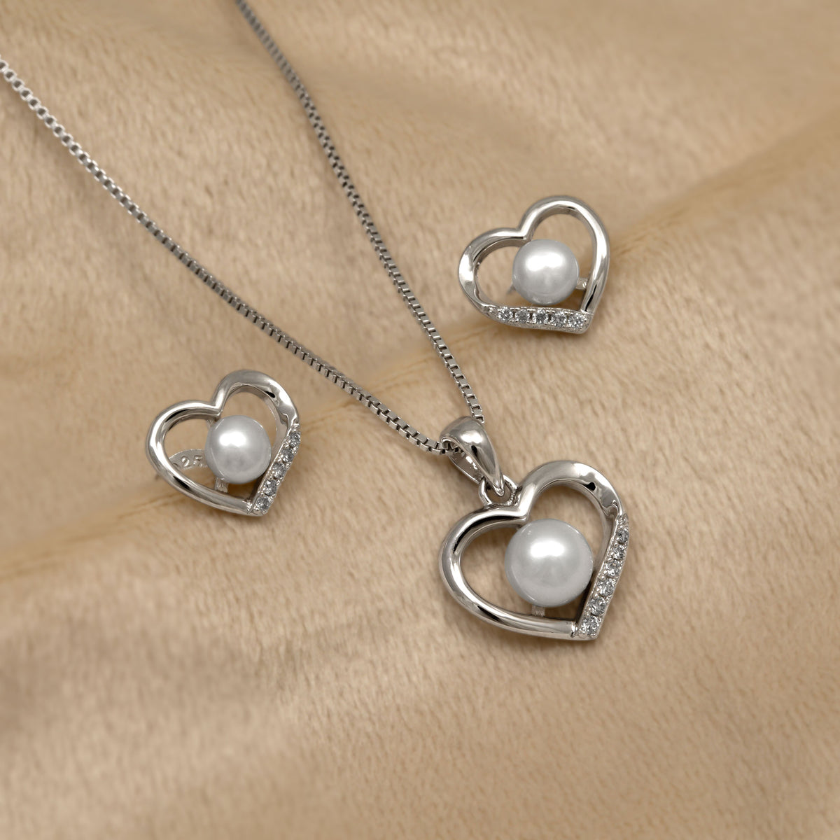 Silver heart-shaped pendant and earring set with pearls and lab grown diamonds on a beige background