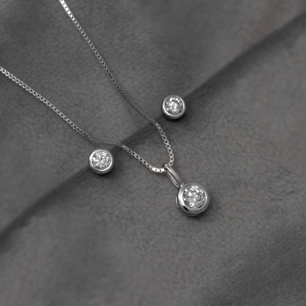 A pair of round bezel-set lab diamond stud earrings and matching diamond pendant in sterling silver, shown on a plain white background.