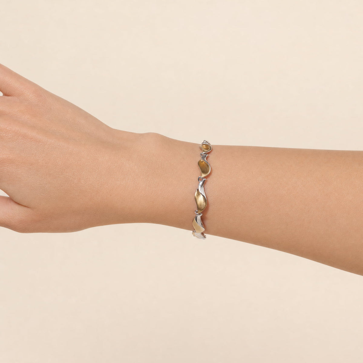 A two-tone bracelet with gold vermeil and silver wave links, shown worn on a person's wrist against a solid beige background.