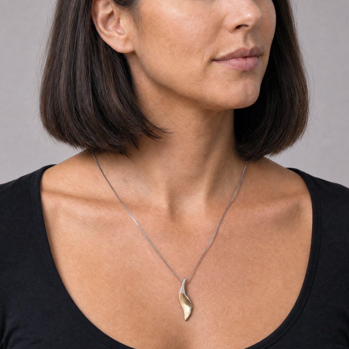 A close-up of a woman wearing a delicate silver necklace with a polished, abstract leaf-shaped pendant in a gold vermeil and silver two-tone finish.