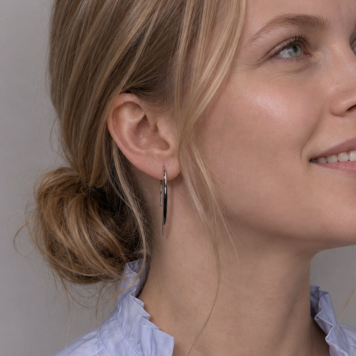 A model wears a pair of minimalist, polished silver drop earrings with a sleek, curved shape, shown against a solid white background.