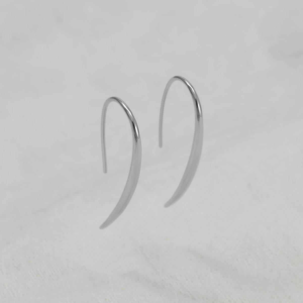 A pair of minimalist, polished silver crescent-shaped earrings on a white background.