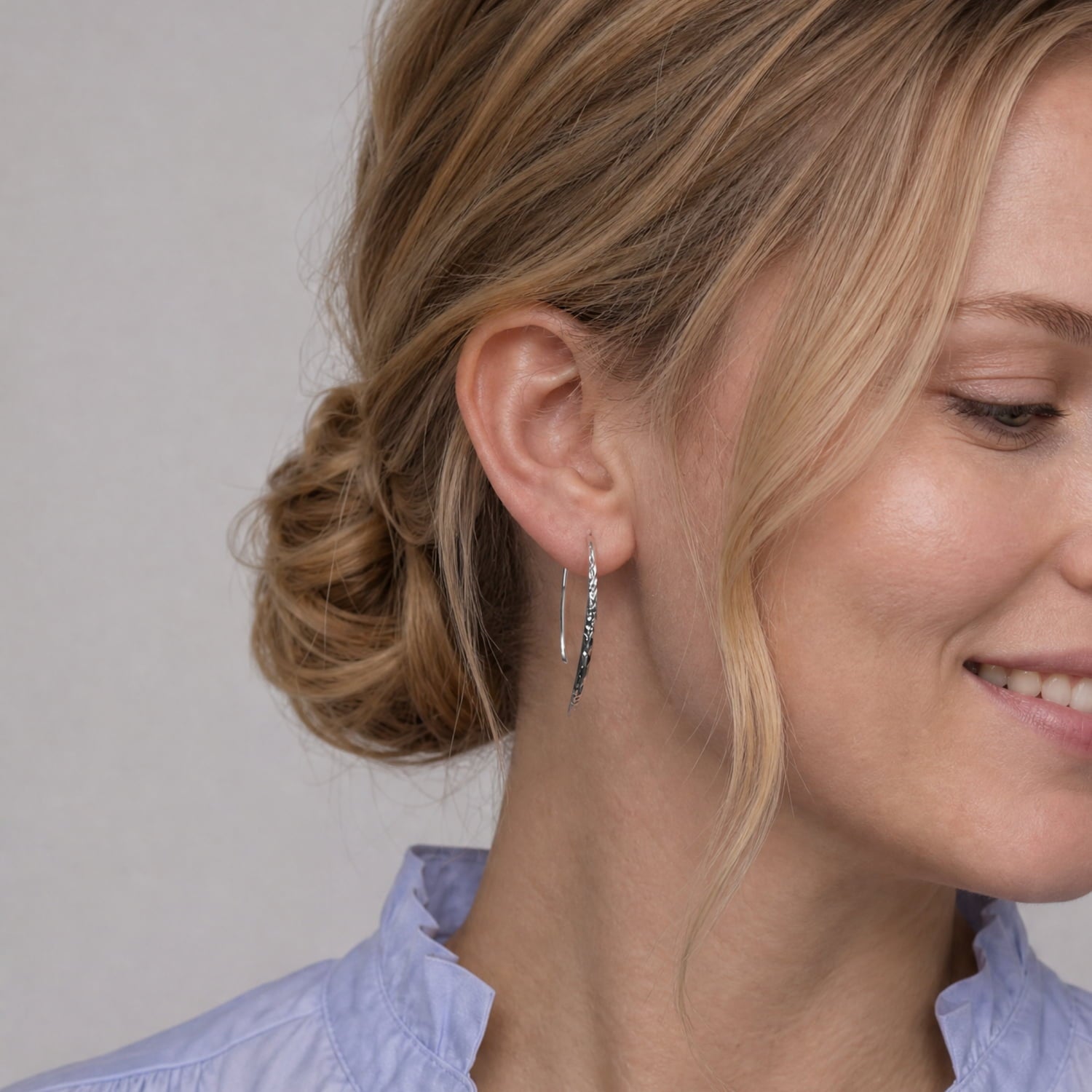 A close up of a model wearing a pair of sterling silver hammered drop earrings with fishhook backs.