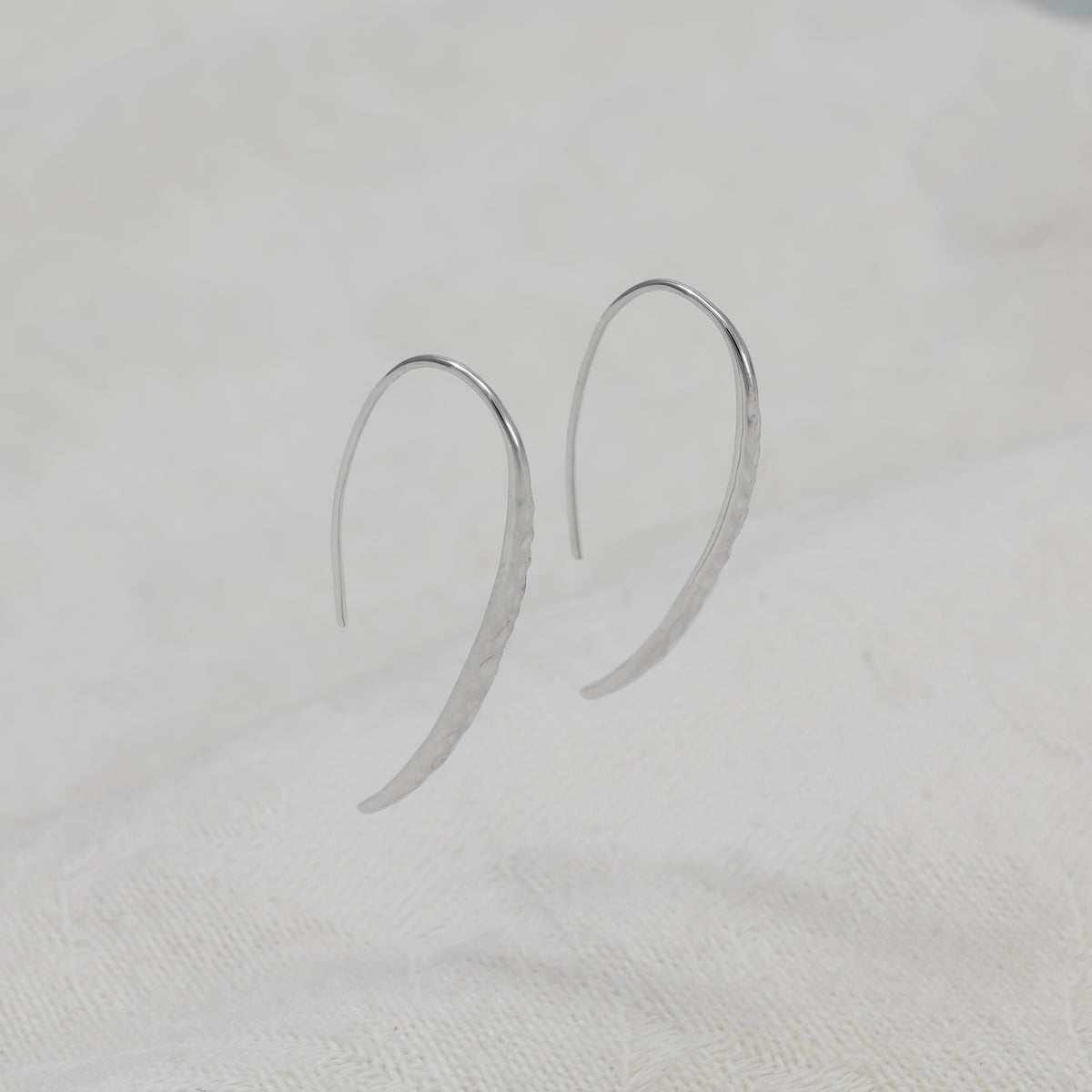 A pair of sterling silver hammered drop earrings with fishhook backs.