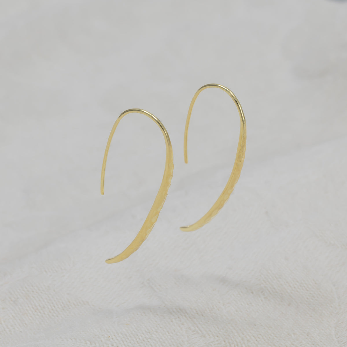 A pair of gold vermeil, hammered drop earrings with a curved, teardrop-like shape and fishhook backings.