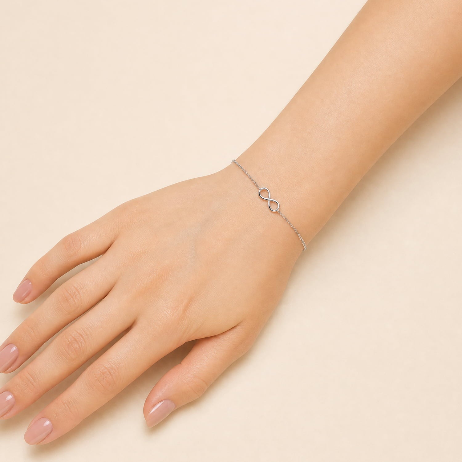 A delicate sterling silver bracelet featuring a simple infinity symbol on a fine chain, worn on a wrist against a plain cream background.