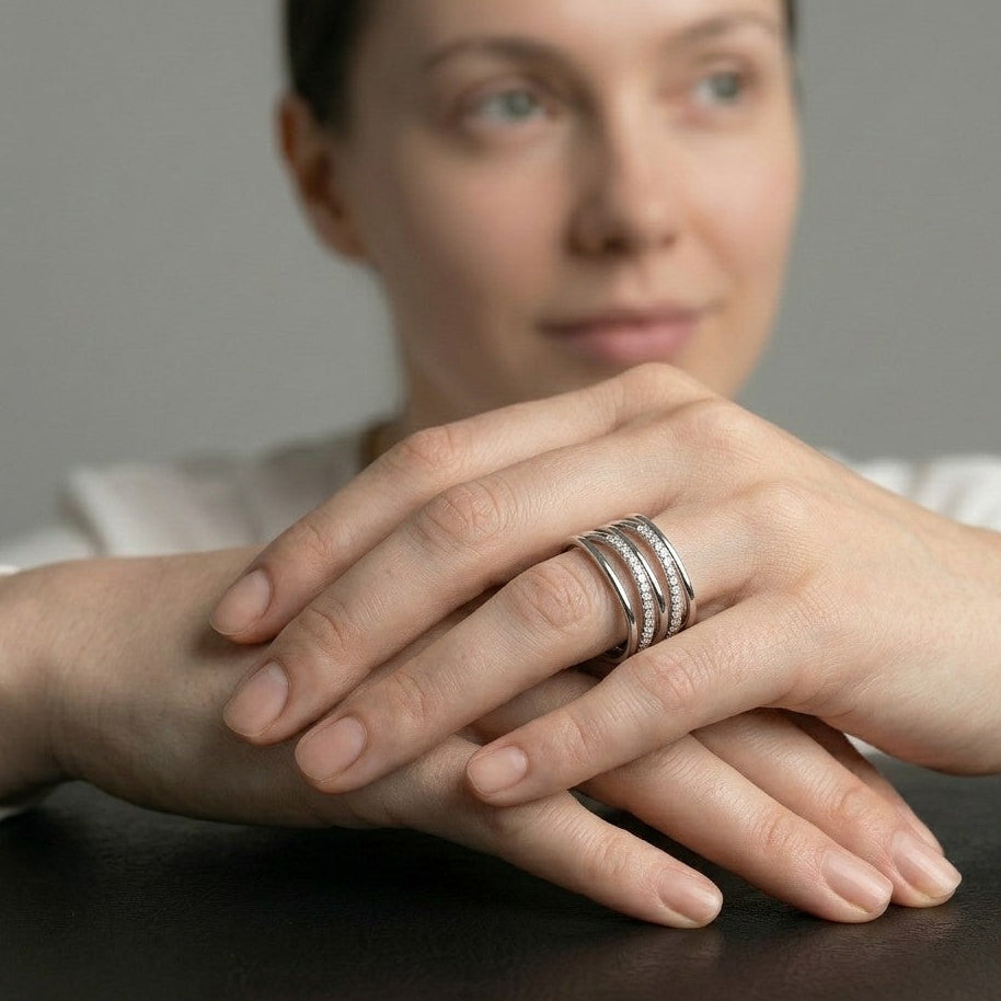 Close-up of a woman's hands resting gently together, showcasing a sterling silver multi-strand ring with pavé detailing that creates a layered wave effect, exemplifying contemporary silver jewellery by a British designer.