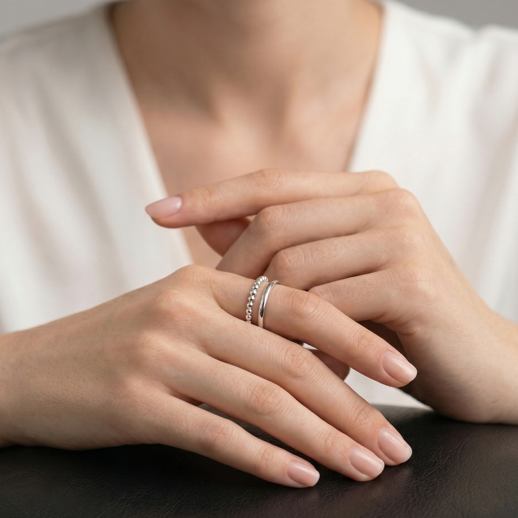Close-up of a person's hands with silver rings on a neutral background