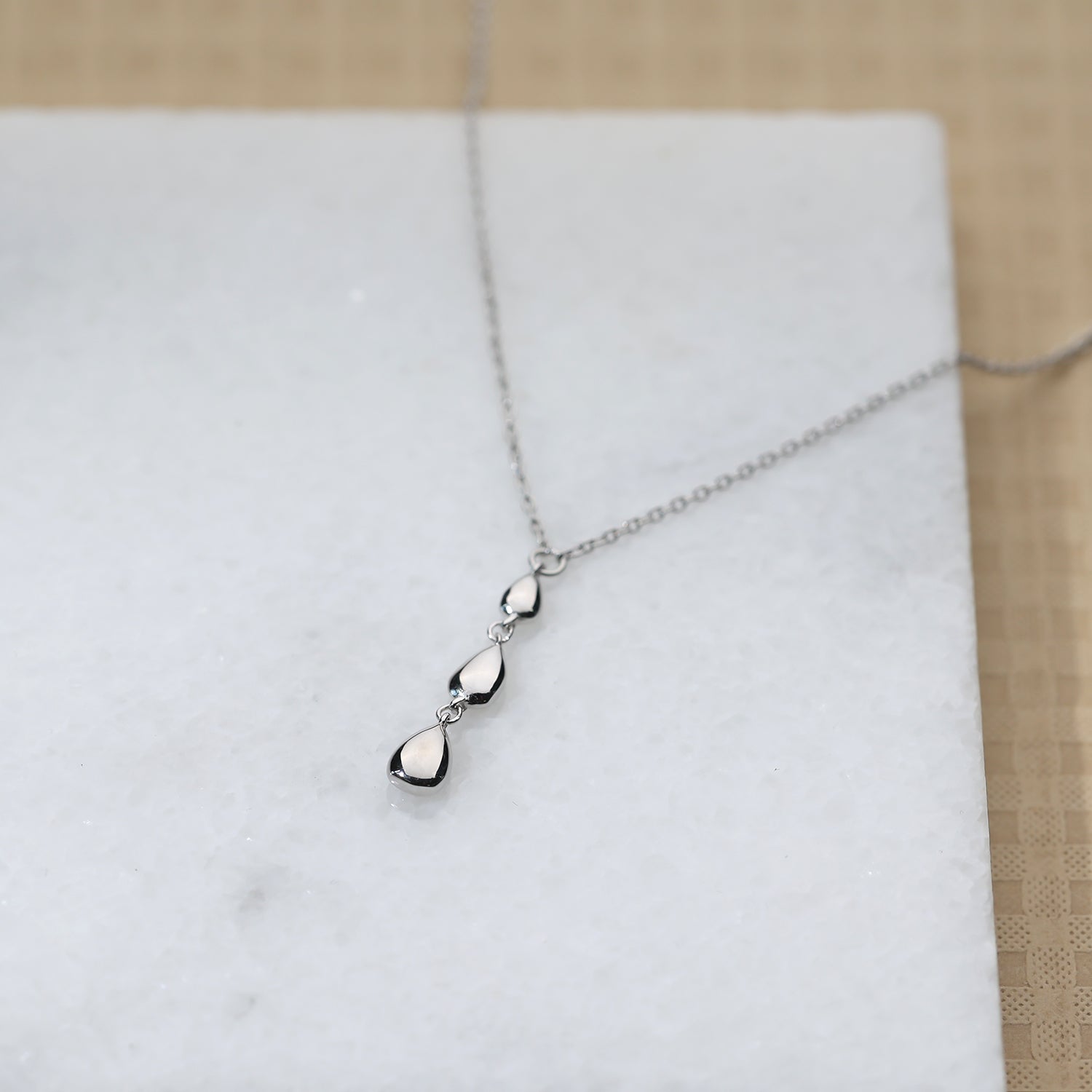 A polished sterling silver necklace featuring a sculptural pendant composed of three connected teardrop shapes, displayed on a white marble surface.