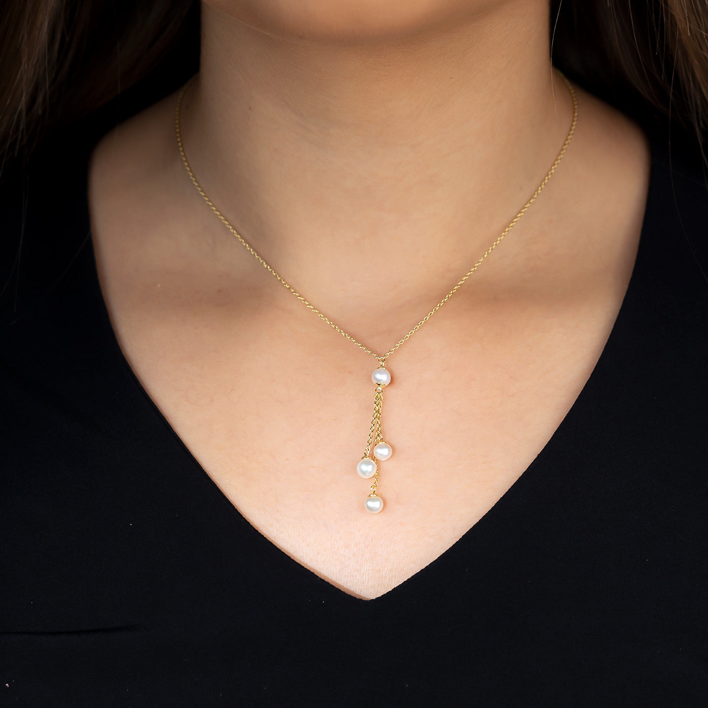 A delicate gold vermeil necklace featuring a pendant with four lustrous pearls arranged on fine chains, worn on a woman’s neck against a black top.