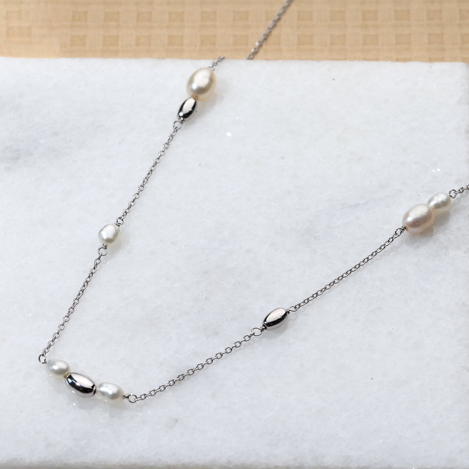 A delicate sterling silver necklace featuring alternating freshwater pearls and polished silver beads arranged along a fine chain, displayed on a light marble surface.