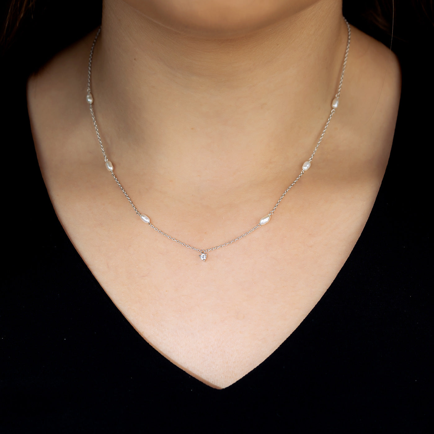 A delicate sterling silver chain necklace featuring small freshwater pearls spaced evenly with a single cubic zirconia charm at the center, worn on a smooth neckline.