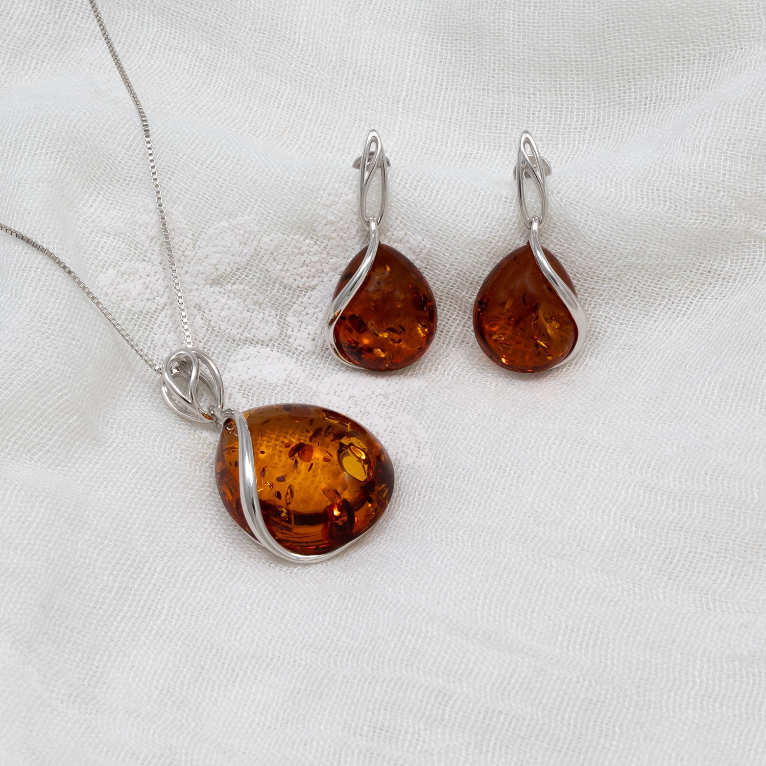 Sterling silver drop earrings featuring large amber teardrop gemstones with sculptural silver wrapping, paired with a matching pendant necklace on a fine silver chain.