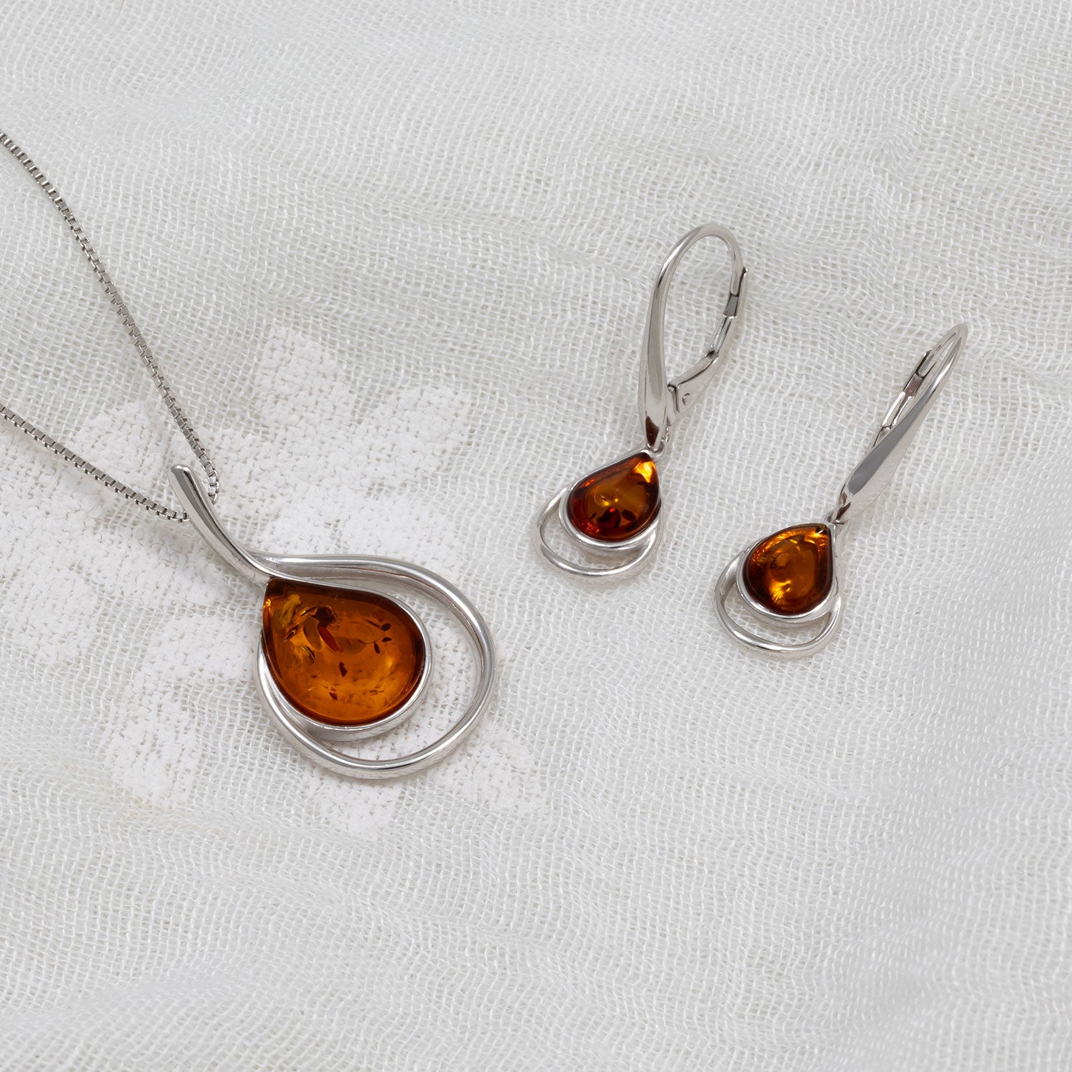 Sterling silver drop earrings and matching pendant featuring curling teardrop-shaped amber stones, showcasing elegant and contemporary British jewellery design.