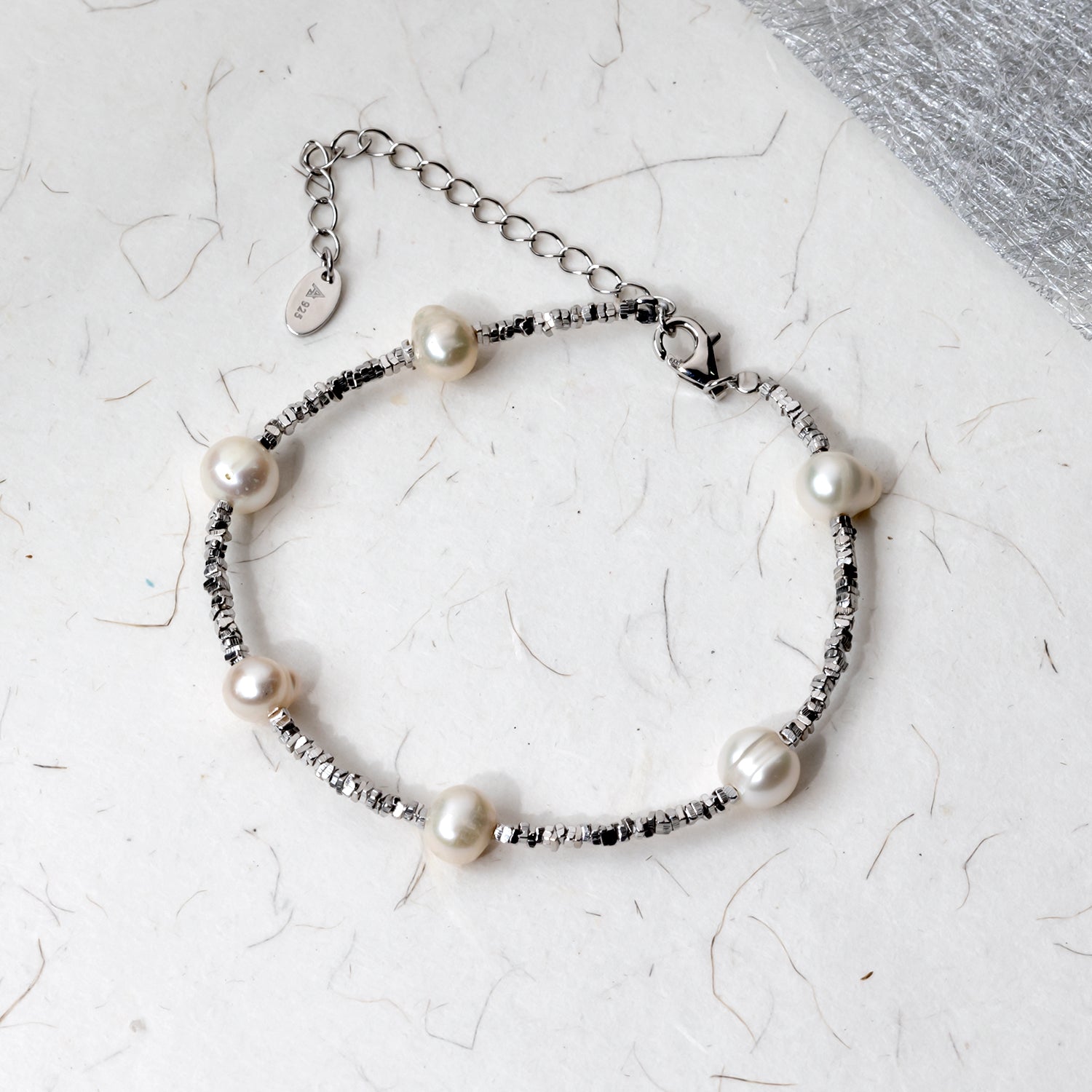 Sterling silver bracelet featuring textured cubed beads interspersed with lustrous freshwater pearls, displayed on a natural textured surface with an adjustable clasp.