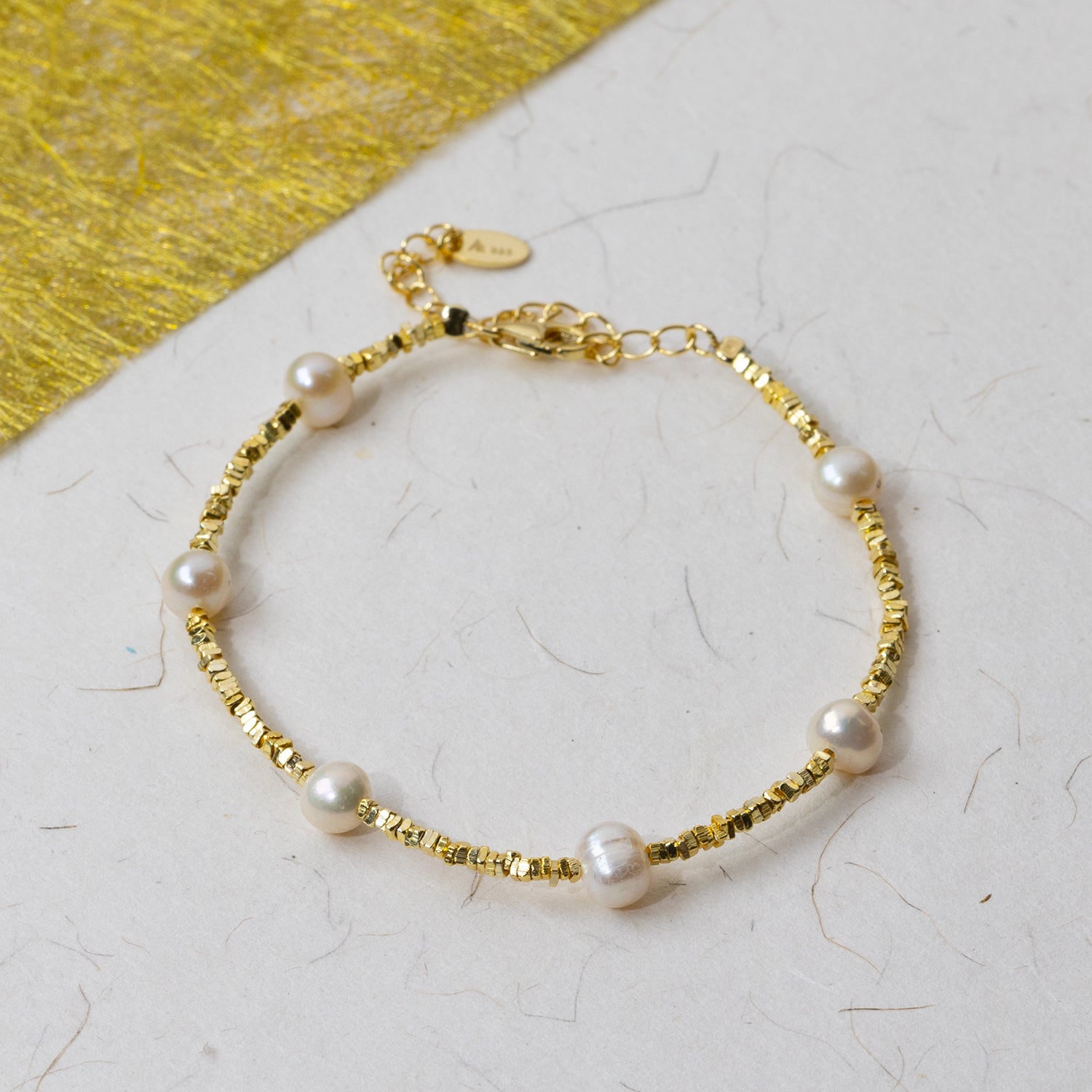 Delicate gold vermeil bracelet featuring small polished cubed beads interspersed with lustrous freshwater pearls, displayed on a textured light background.