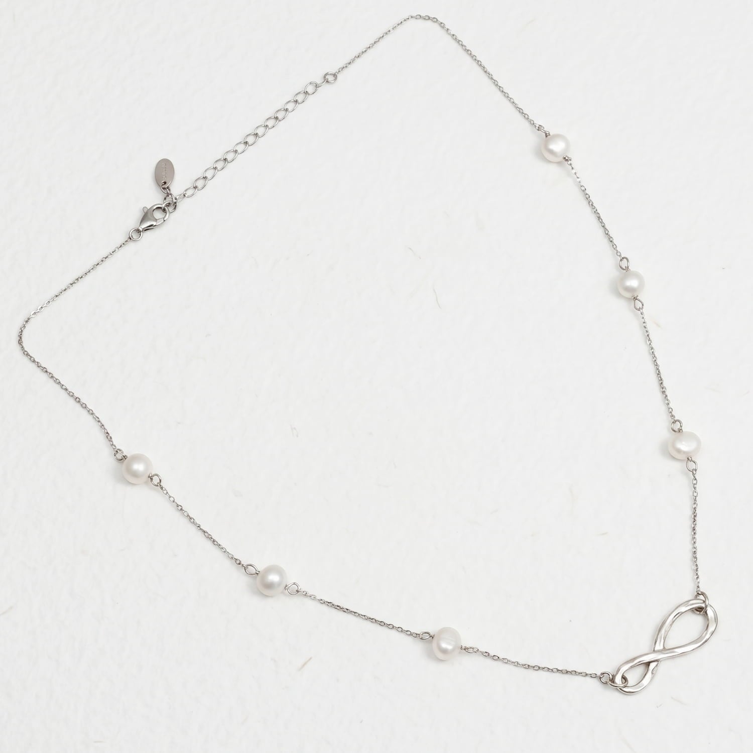 Sterling silver necklace featuring a polished infinity symbol pendant with evenly spaced freshwater pearls along a delicate chain, set against a white background.