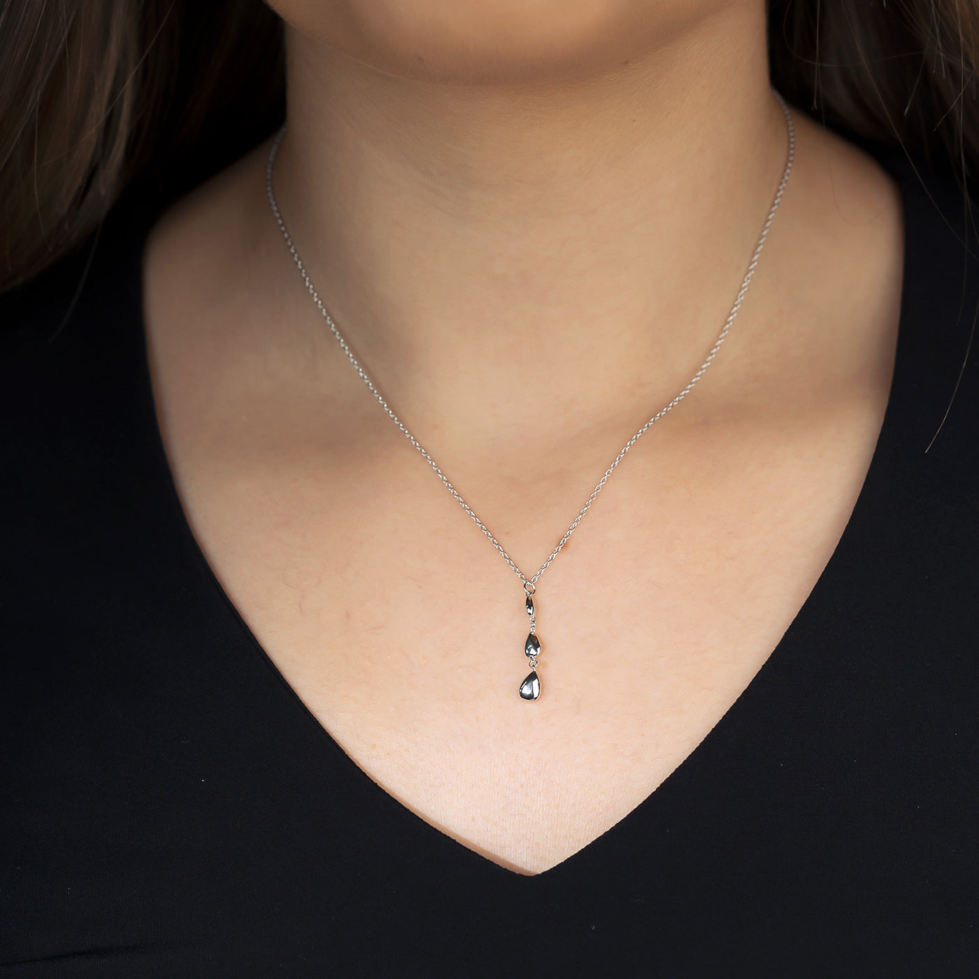 A polished sterling silver pendant featuring three teardrop-shaped elements hanging vertically from a delicate chain, worn on a black V-neck top.
